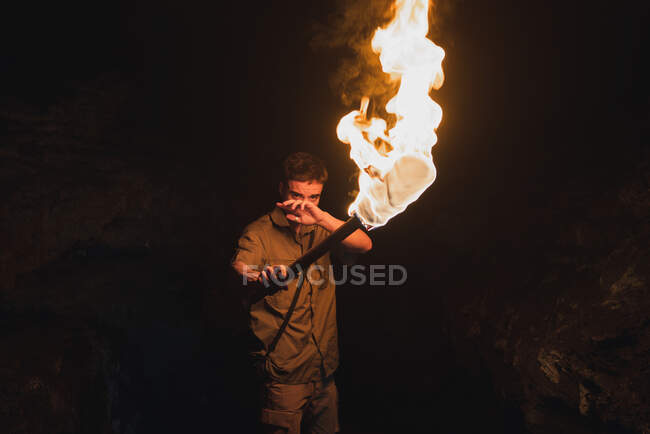 Молодий чоловічий спелеолог з палаючим факелом, що стоїть у темній вузькій скелястій печері, досліджуючи підземне середовище — стокове фото