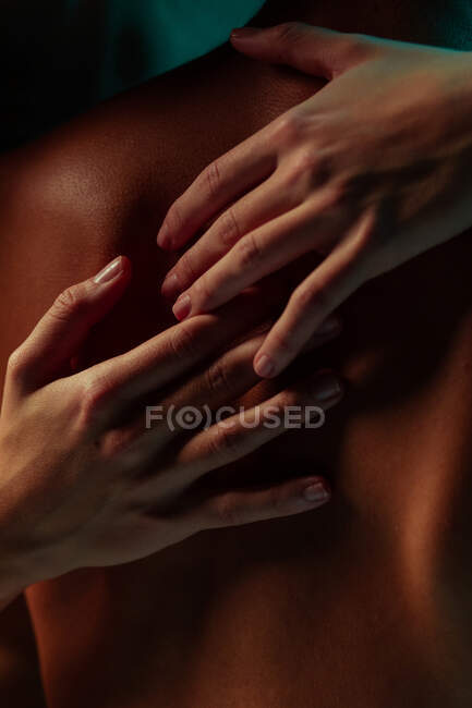 Mulher mãos abraçando um homem de volta sob luzes de cor — Fotografia de Stock