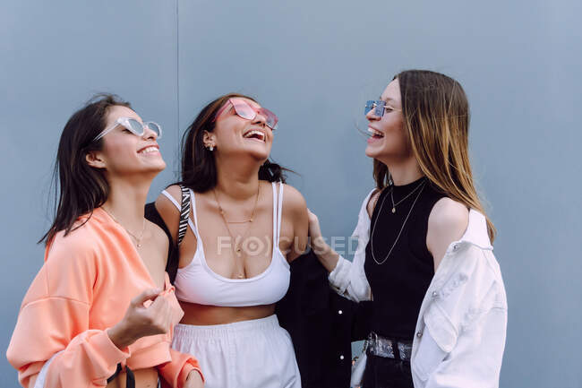 Amis féminines positives dans des lunettes de soleil à la mode et des vêtements décontractés riant joyeusement tout en passant du temps agréable ensemble — Photo de stock