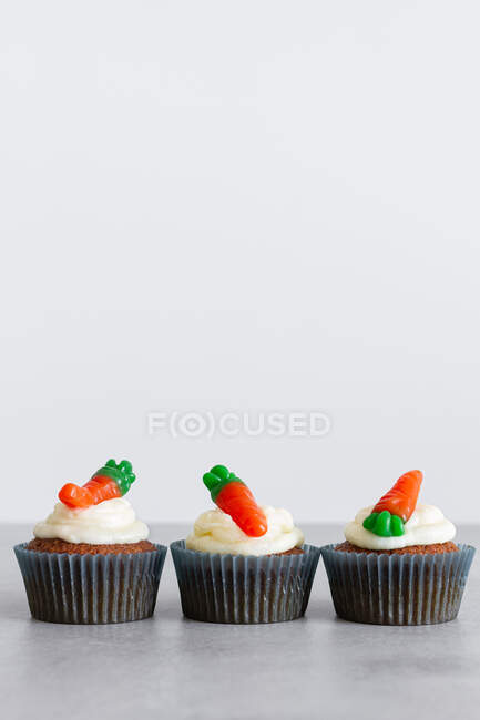 Filas de dulces deliciosos cupcakes de zanahoria con crema tierna y gomitas en forma de zanahoria en la superficie gris - foto de stock