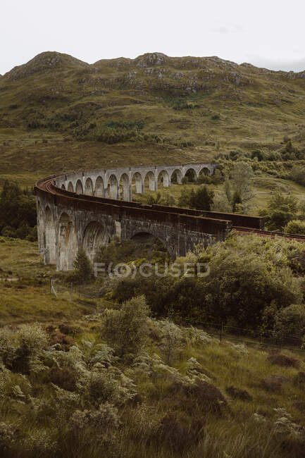 Alte Eisenbahnstrecke entlang der alten Bogenbrücke in der Nähe des rauen Hügels an einem grauen Tag in Glenfinnan, Großbritannien — Stockfoto