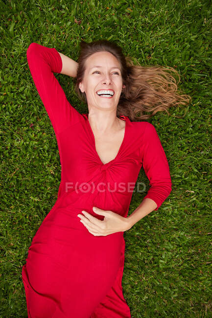 Woman dressed in red lying on the ground in a park with grass — Stock Photo