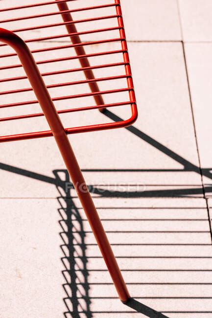 Silla de metal roja al aire libre de verano colocada en el suelo blanco a la luz del sol con sombra - foto de stock