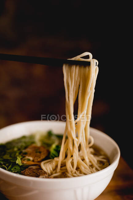 Tasty beef ramen in ceramic white bowl with chopsticks pulling long noodles — Stock Photo
