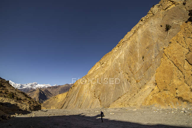 Vista lejana del viajero parado en el lecho del río seco en la cordillera del Himalaya bajo el cielo azul en Nepal - foto de stock