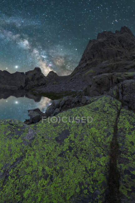 Spectacular mountain landscape with rocky peaks and shiny Milky Way in night sky reflected in lake water — Stock Photo