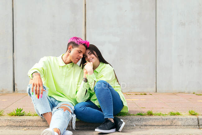 Gay man with pink hair and smiling woman sitting in street and holding hands — Stock Photo