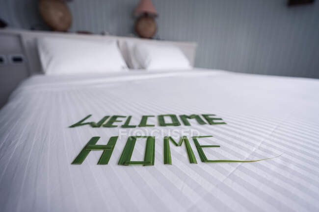 Maldives hotel room with bed in white sheets with letters made of bamboo leaves written welcome home — Stock Photo