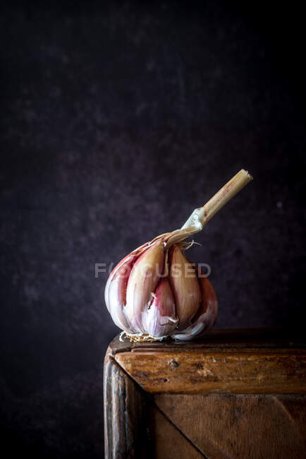 Cabeza entera de ajo fresco colocada sobre una mesa de madera en una cocina rústica con fondo oscuro - foto de stock