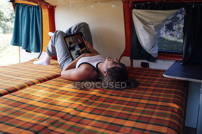 Calmo explorador do sexo feminino deitado na cama em van e navegar na Internet em tablet durante a viagem de verão — Fotografia de Stock