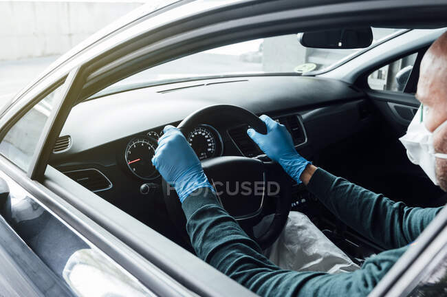 Vista laterale dell'uomo irriconoscibile ritagliato che utilizza una maschera protettiva che guida l'auto durante la quarantena — Foto stock
