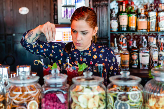 Barman féminin concentré garnissant des cocktails frais dans des verres placés sur le comptoir dans le bar — Photo de stock