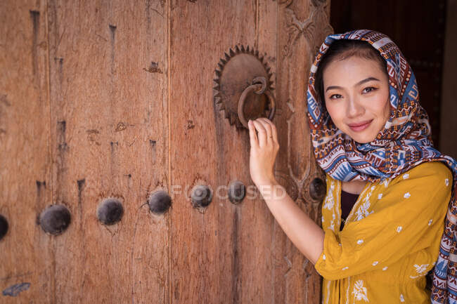 Mulher asiática com lenço de cabeça ao lado de uma velha porta de madeira — Fotografia de Stock