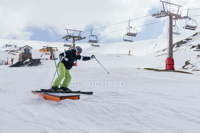 Atleta masculino anónimo en máscara de tela cabalgando en esquí sobre nieve contra Sierra Nevada y teleférico en España - foto de stock