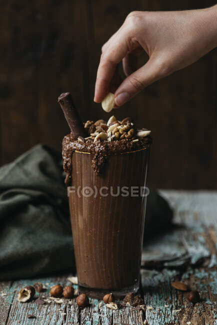 Unrecognizable person throwing some nuts over vegan smoothie in dark scene — Stock Photo