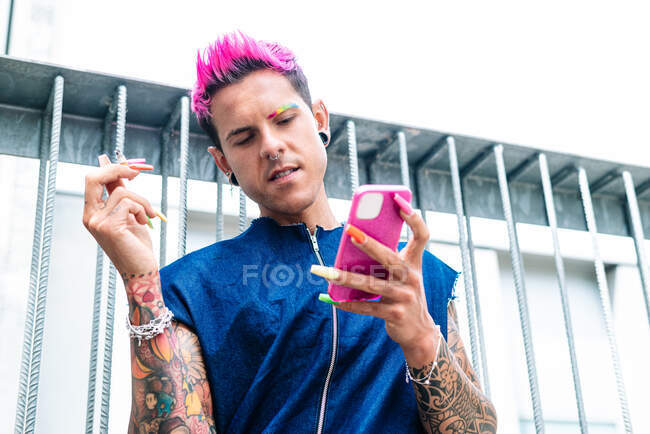 Trendiger homosexueller Mann mit pinkfarbenen Haaren und bunten dicken Nägeln, der auf der Straße Selbstaufnahmen mit dem Smartphone macht — Stockfoto