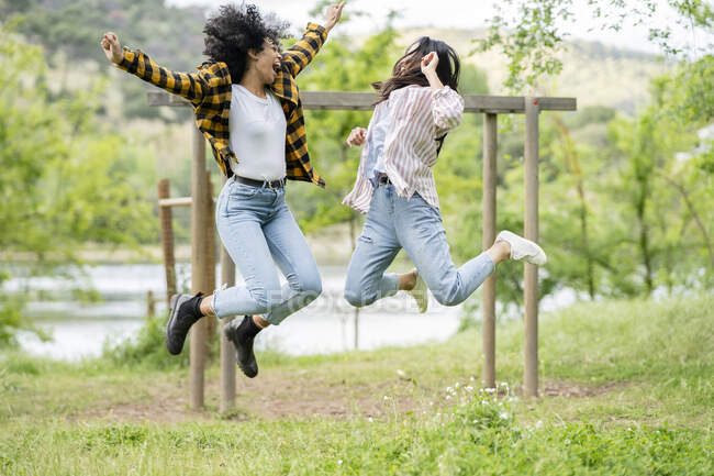Пара лесбійських багатоетнічних жінок стрибають над землею в лісі і насолоджуються свободою разом — стокове фото