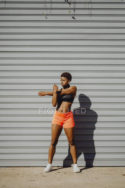 Young fitness African American woman stretching arms before running on city street — Stock Photo