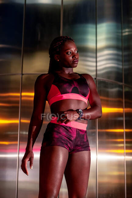 Sportiva afroamericana pensierosa in piedi al muro di metallo e guardando lontano di notte — Foto stock