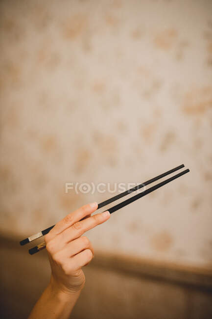 Mano de mujer sosteniendo palillos de bambú asiáticos tradicionales sobre fondo moteado beige - foto de stock