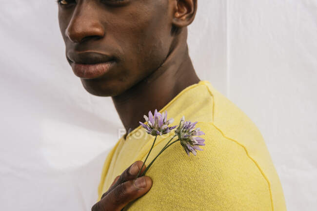 Cortado irreconocible hombre afroamericano con ramo de flores silvestres mirando a la cámara sobre fondo blanco - foto de stock