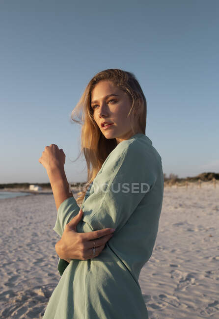 Femme blonde aux cheveux longs debout sur la plage regardant au loin — Photo de stock