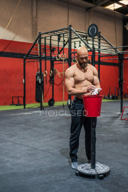 Muscular bearded guy in sportswear clapping hands and spreading powder during bodybuilding workout in gym — Stock Photo