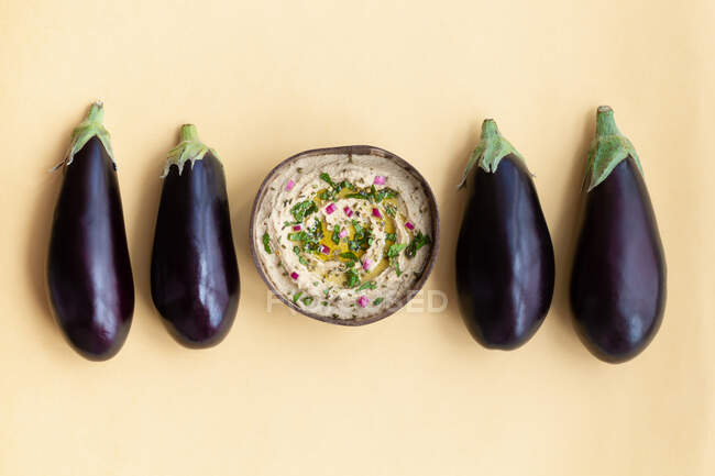 Top view of fresh ripe aubergines placed on beige table with bowl of appetizing traditional Baba ghanoush dish — Stock Photo
