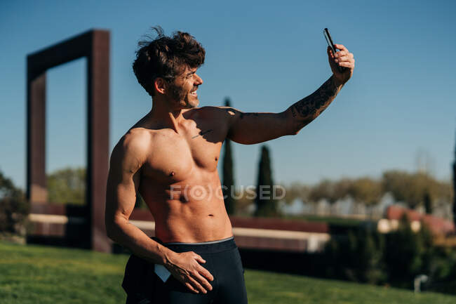 Веселий чоловічий спортсмен з голим торсом взяв собі портрет на мобільний телефон після тренування в сонячний день — стокове фото