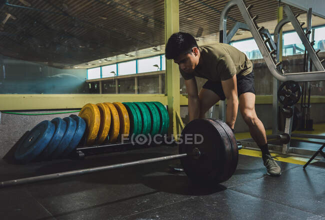 Focused Asian male athlete doing deadlift with heavy barbell during workout in gym — Stock Photo