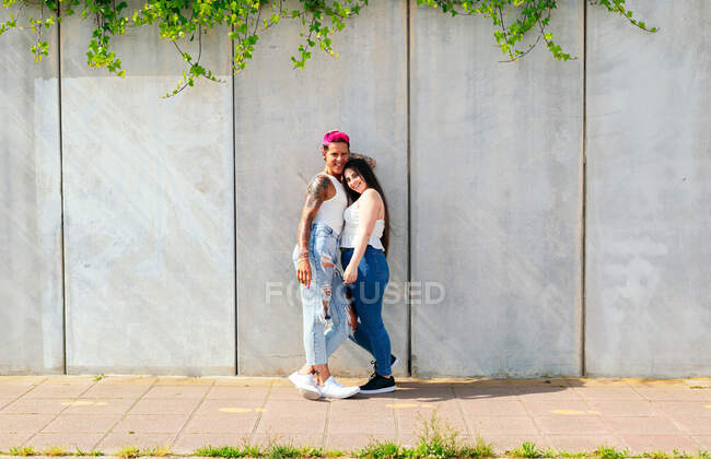 Conteúdo macho homossexual com cabelo rosa e mulher amigável em pé perto da parede na cidade e olhando para a câmera — Fotografia de Stock