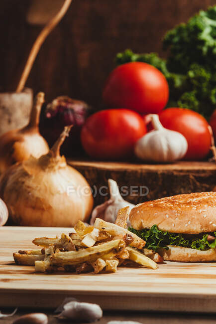Appetizing hamburgers with vegetables placed on wooden board with French fries in kitchen — Stock Photo