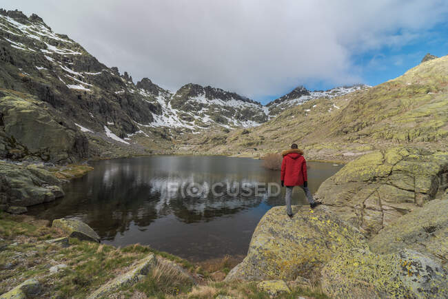 Rückansicht eines anonymen Mannes in Oberbekleidung, der auf Steinen in der Nähe des Laguna Grande Sees inmitten der Berge der Sierra de Gredos in Avila, Spanien, steht — Stockfoto