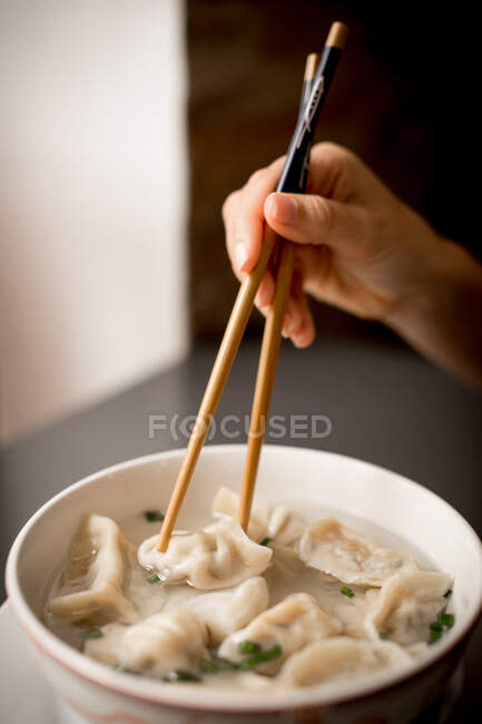 Mano de mujer con palillos asiáticos tradicionales comiendo sopa de albóndigas en tazón de cerámica - foto de stock