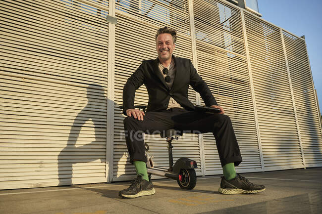 Homem de negócios sentado em sua bicicleta elétrica fora do prédio de escritórios na hora do pôr do sol — Fotografia de Stock