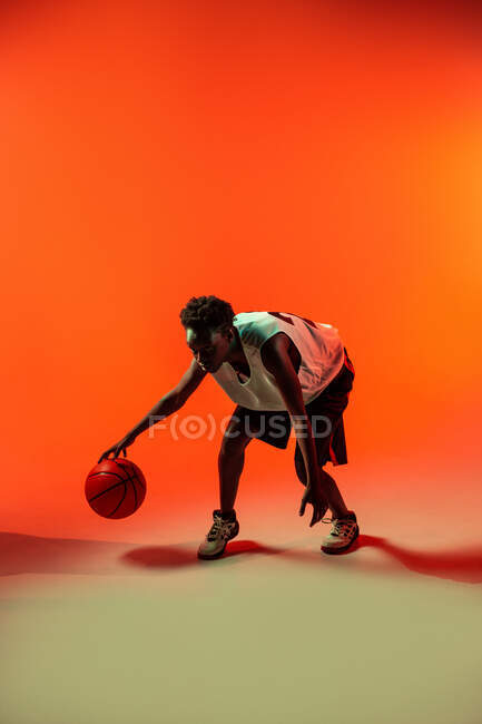 Чорна жінка з баскетбольним вбранням в студії з використанням кольорових гелів і проекторних вогнів на помаранчевому фоні — стокове фото