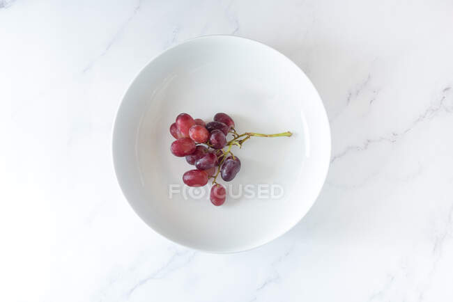 Von oben von einem Bund süßer rosa Trauben, serviert auf einem Teller auf weißem Hintergrund — Stockfoto