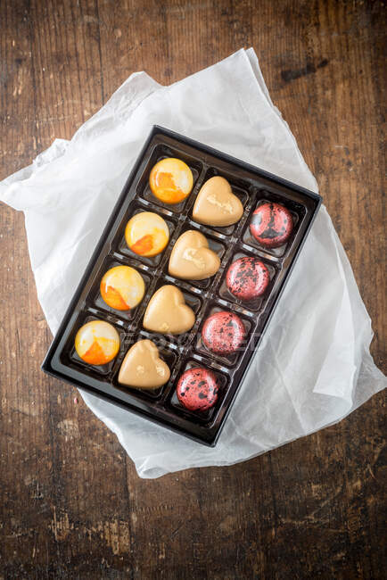Вид зверху на солодкі барвисті шоколадні цукерки в коробці, розміщені на дерев'яному столі — стокове фото
