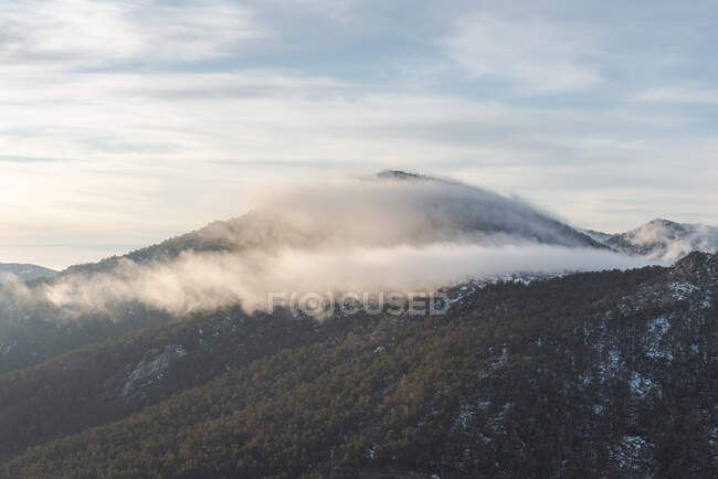 Crête de montagne couverte de neige et de forêt verte située contre un ciel nuageux le matin dans le parc national de la Sierra de Guadarrama à Madrid, Espagne — Photo de stock