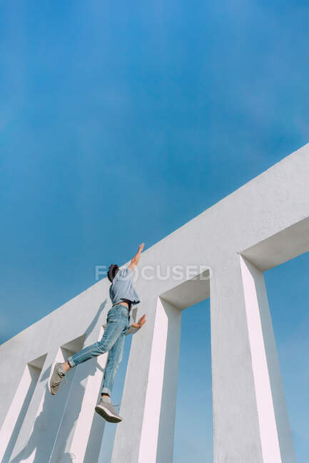 From below of anonymous fearless male hanging on edge of concrete wall and showing risky parkour trick — Stock Photo