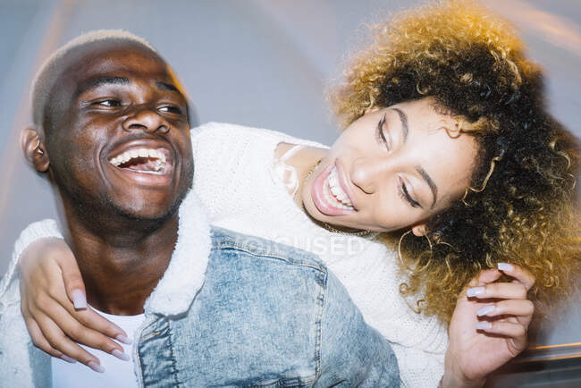 Веселий молодий афроамериканець їде до щасливої подружки з кучерявим волоссям у модному одязі біля морозяного світла. — стокове фото