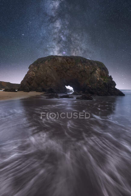 Сценический вид на скалы на пляже возле моря под захватывающим ночным звездным небом в длительной экспозиции — стоковое фото