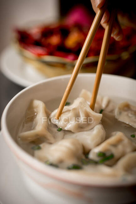 Рука жінки з традиційними азіатськими паличками, що їдять суп з пельменів у керамічній мисці — стокове фото