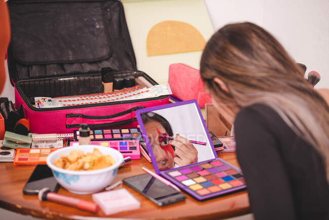 Молодая женщина смотрит на зеркало и рисует орнамент на лице, нанося творческий макияж в студии — стоковое фото