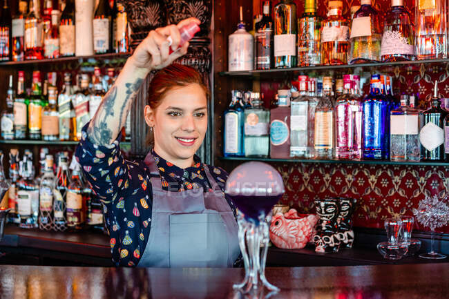 Delizioso barista donna in grembiule preparare sapore blaster cocktail al bancone in legno nel bar — Foto stock
