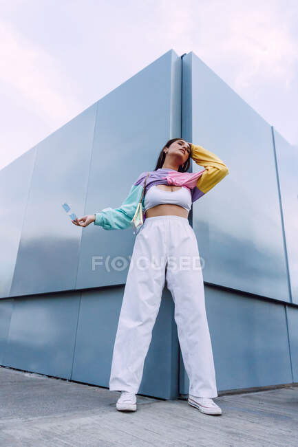 Confident female wearing jeans with top and colorful shirt with stylish sunglasses standing near wall — Stock Photo