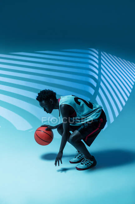 Чорна жінка з баскетбольним одягом у студії використовує кольорові гелі та проектори світла на синьому фоні. — стокове фото