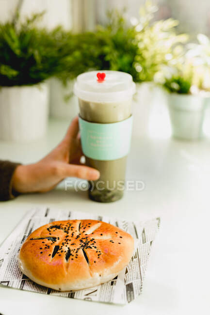Azuki cake placed on table and hand of woman holding plastic cup with beverage — Stock Photo