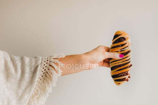 Mãos de mulher com manicure rosa brilhante segurando saboroso pão azuki cozido no fundo cinza — Fotografia de Stock