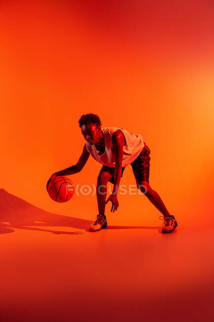 Black woman with basketball outfit in the studio using color gels and projector lights over orange background — Stock Photo